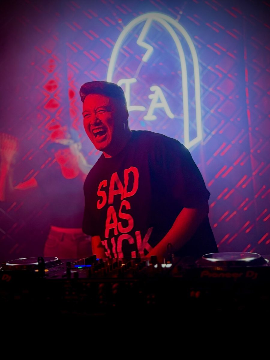 Chef Isaiah Liu laughing behind DJ decks under a neon sign