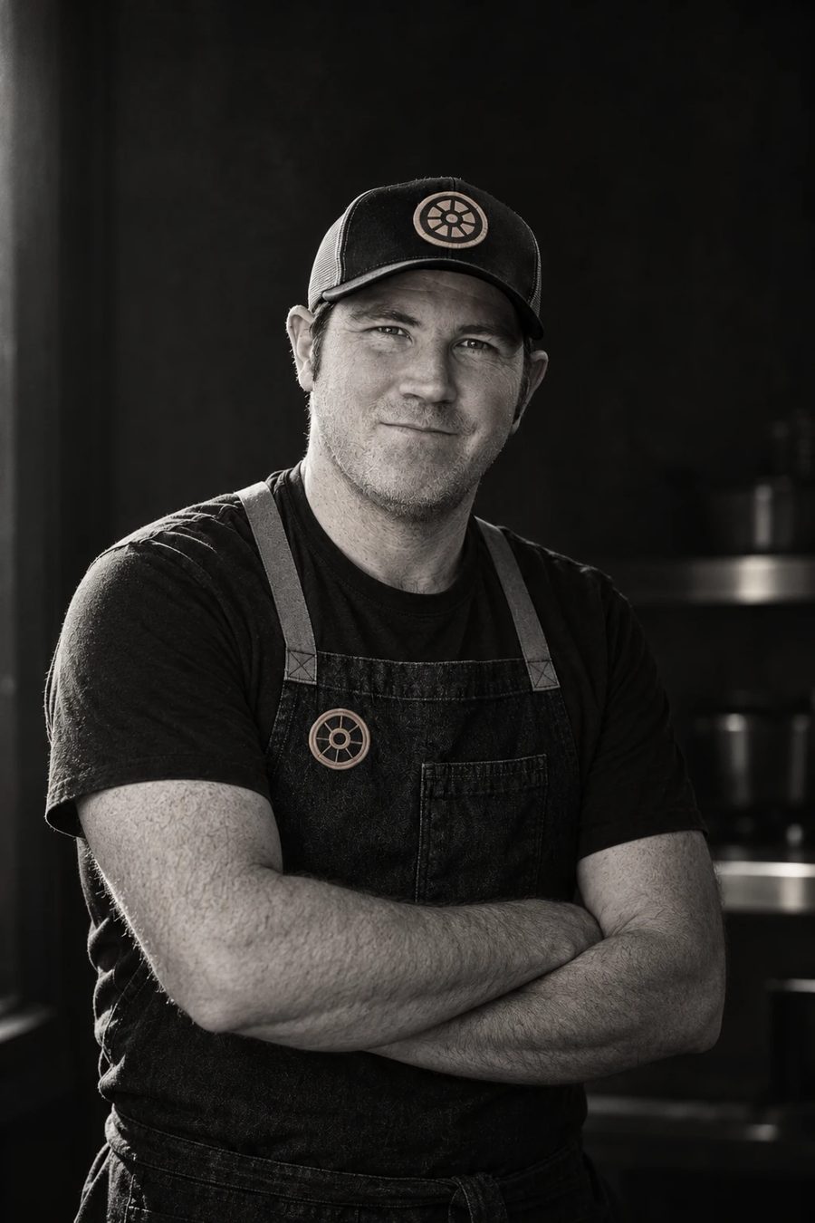 Chef Kris in an apron and an Hmde. cap, arms crossed